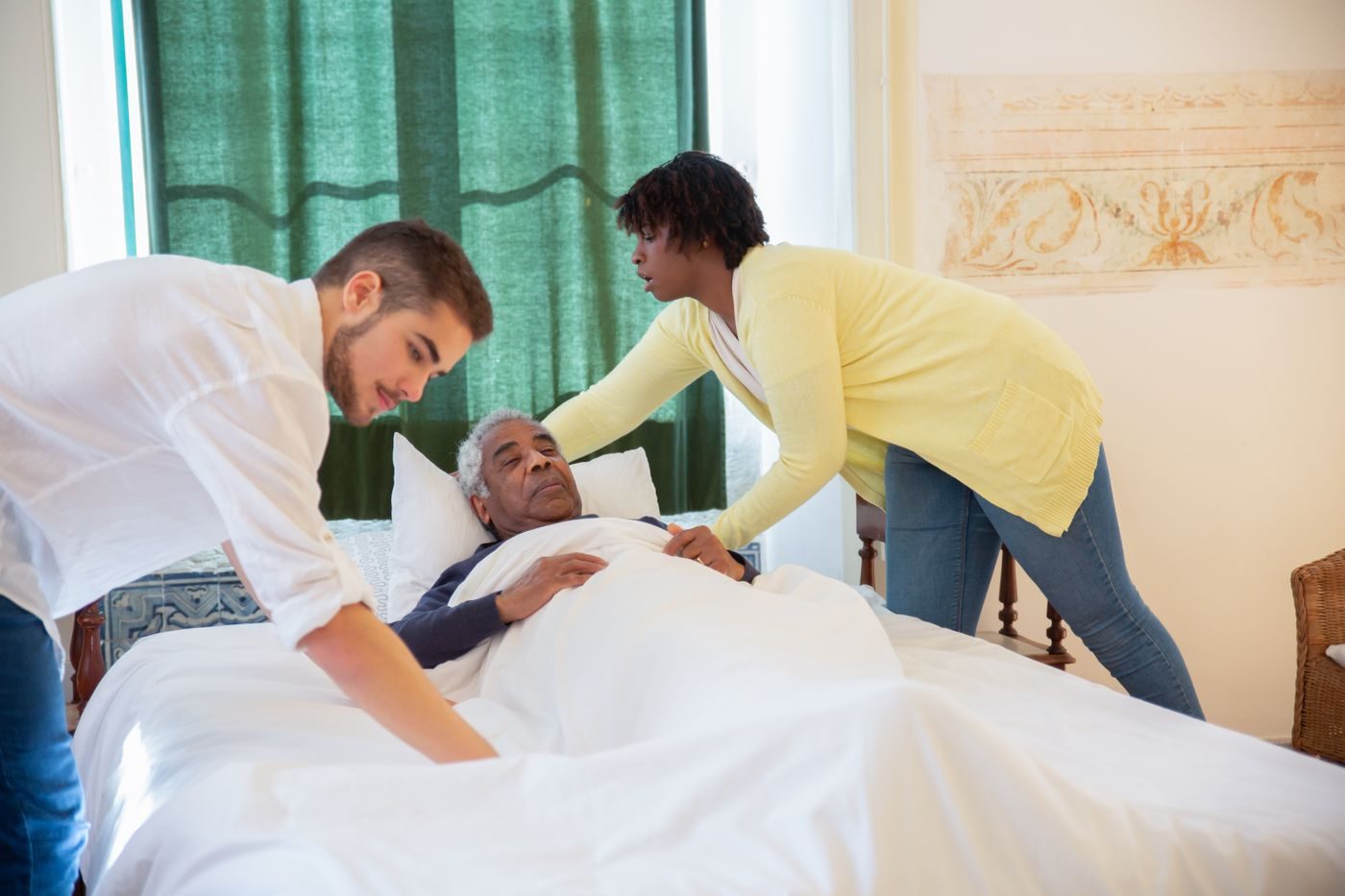 Two caregivers making a client's bed while he rests comfortably